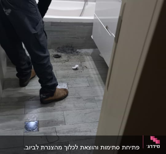 אדם מתקן צנרת ליד אמבטיה בחדר רחצה